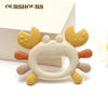 A silicone crab-shaped baby teether in beige and yellow colors is shown on a white background.