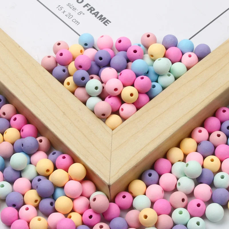 A collection of matte acrylic beads in various pastel colors like pink, purple, blue, and yellow arranged in a wooden frame.