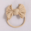 A beige fabric baby bow headband with a soft elastic band.