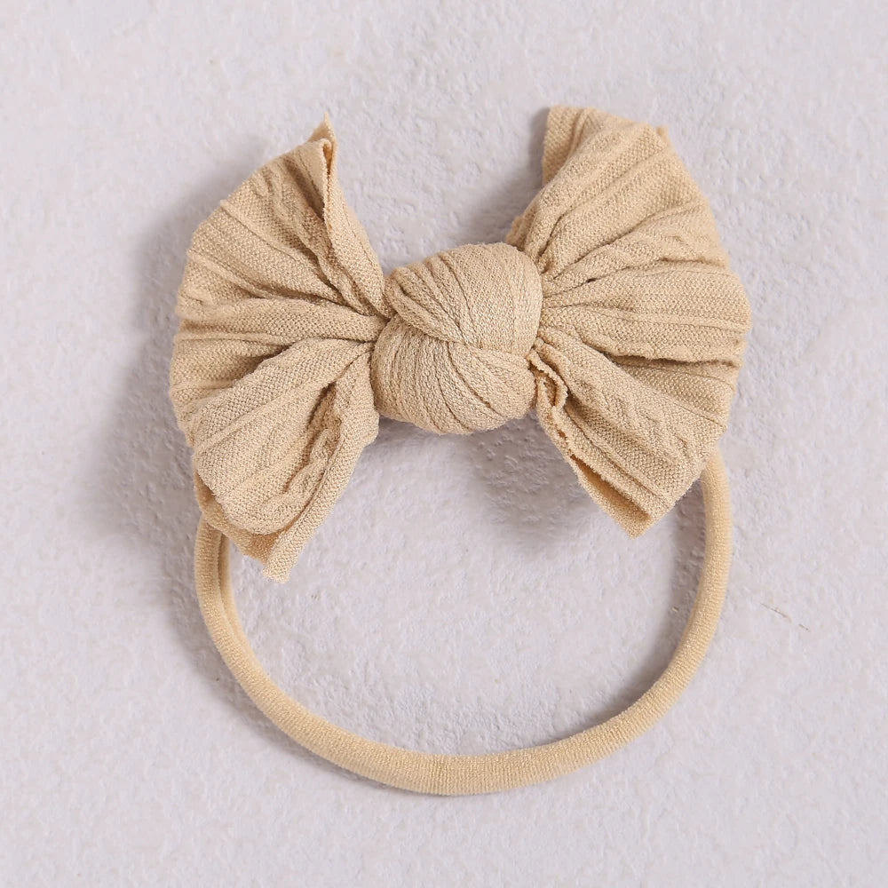 A beige fabric baby bow headband with a soft elastic band.