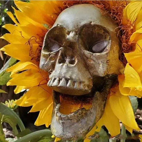 A realistic skull sculpture is placed within a bright yellow sunflower for garden decoration.