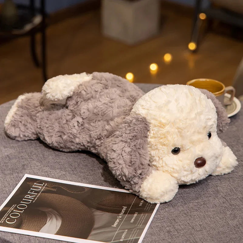 A soft, lying dog plush toy with gray and cream fur resting on a gray fabric surface.