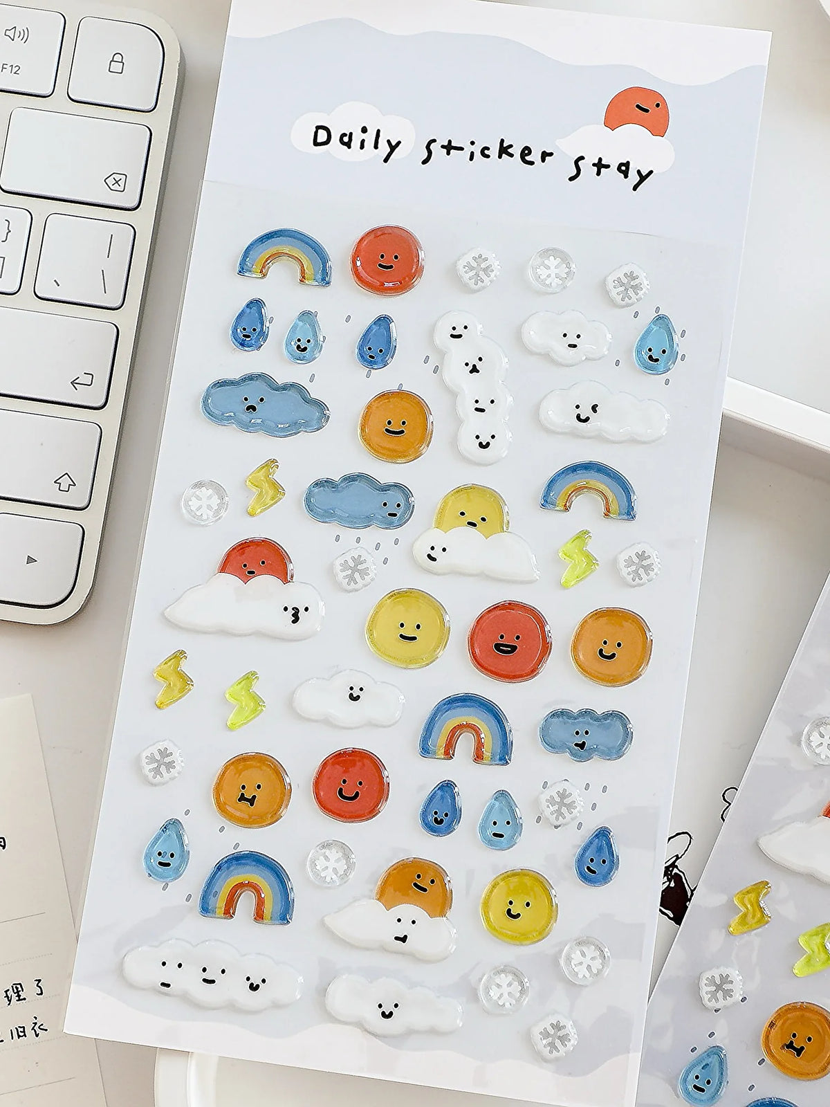 A sheet of white paper filled with various 3D smile face crystal stickers shaped like clouds, rainbows, and other cute elemen