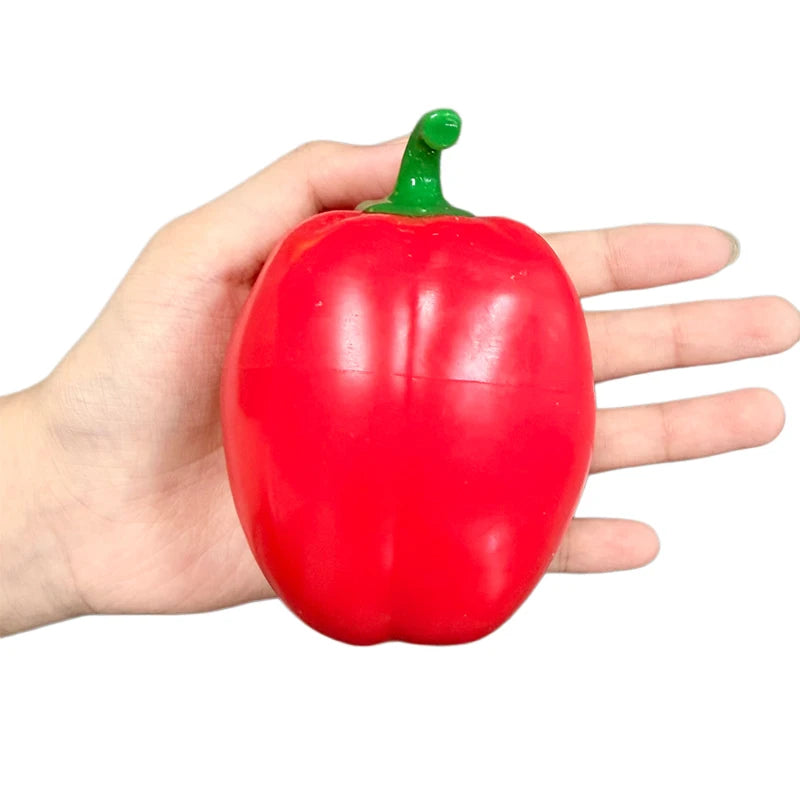 A hand is holding a bright red bell pepper fidget toy with a green stem.