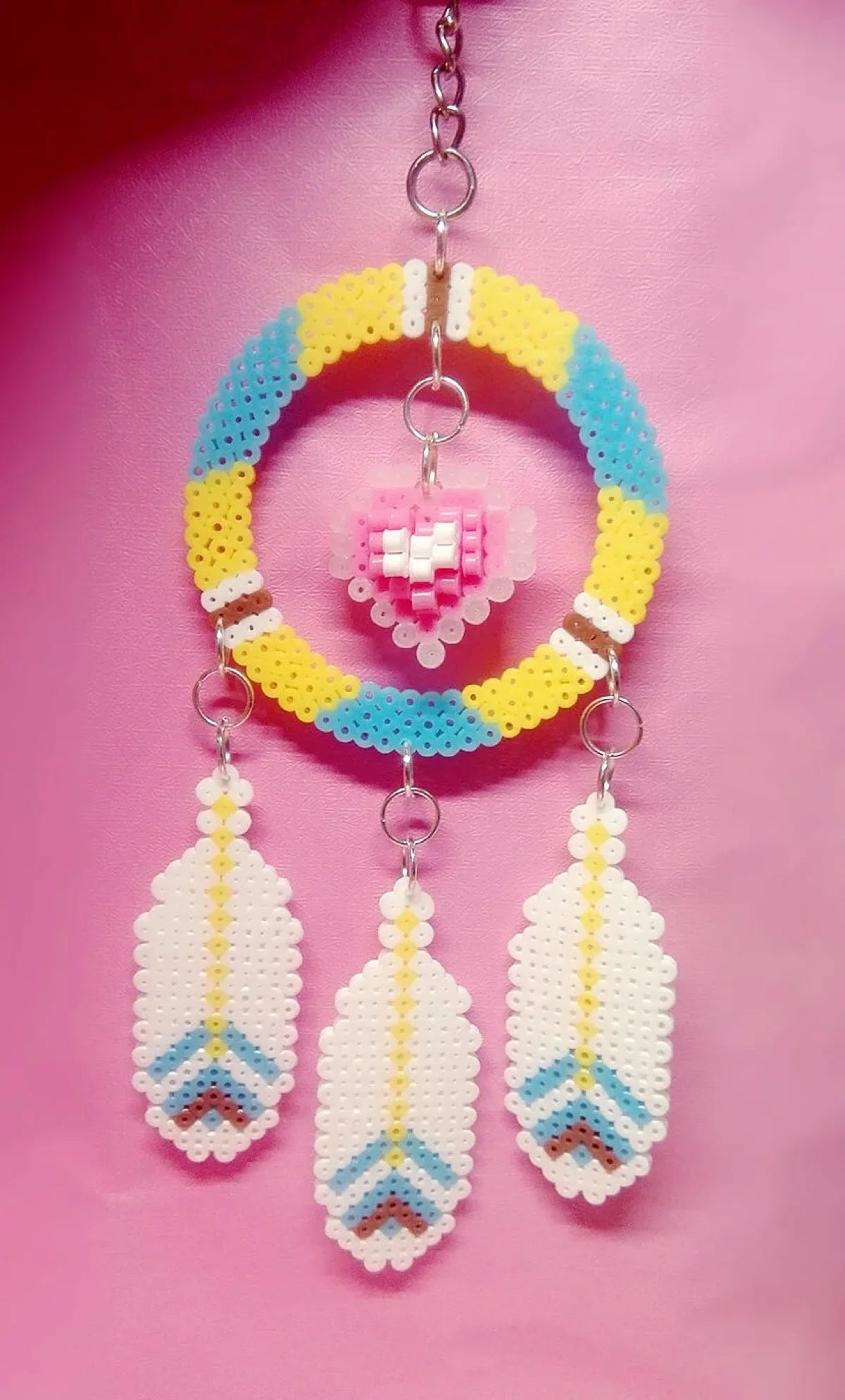 A necklace featuring a circular bead design with yellow, blue, and pink beads, suspended with three white feather-shaped pend