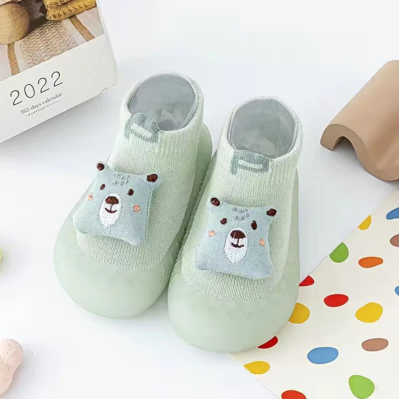 A pair of soft, light green animal-themed socks for babies and toddlers with a fuzzy texture.