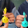 A hand holds a yellow Otamatone mini electronic musical instrument toy against a blurred background.