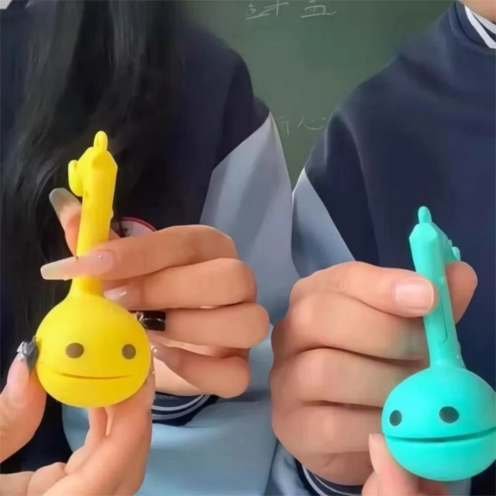 A hand holds a yellow Otamatone mini electronic musical instrument toy against a blurred background.