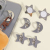 Silver and copper decorative phone charm hooks with adhesive backing arranged on a light surface.