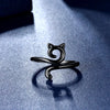 A black adjustable cat-ear crochet ring is displayed on a blue surface with a soft shadow.