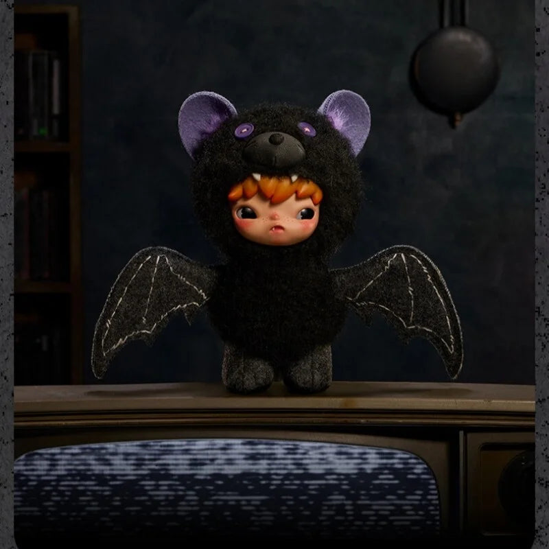 A dark plush doll with purple ears and orange hair has black wings, displayed on a wooden surface.
