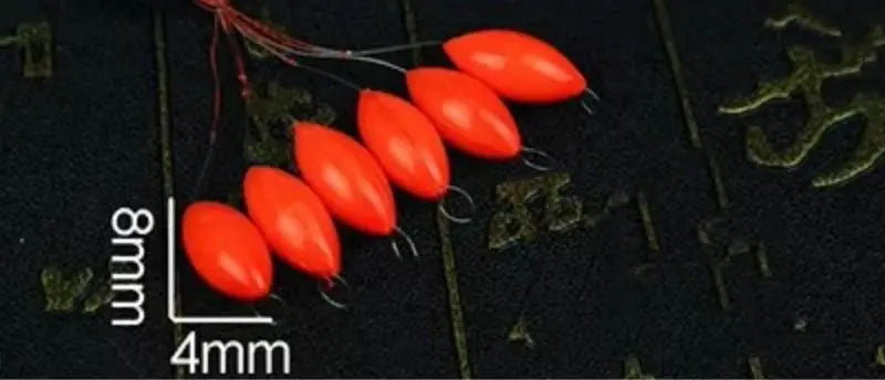 A row of bright orange oval fishing floats with attached bobber beads is displayed on a dark surface.