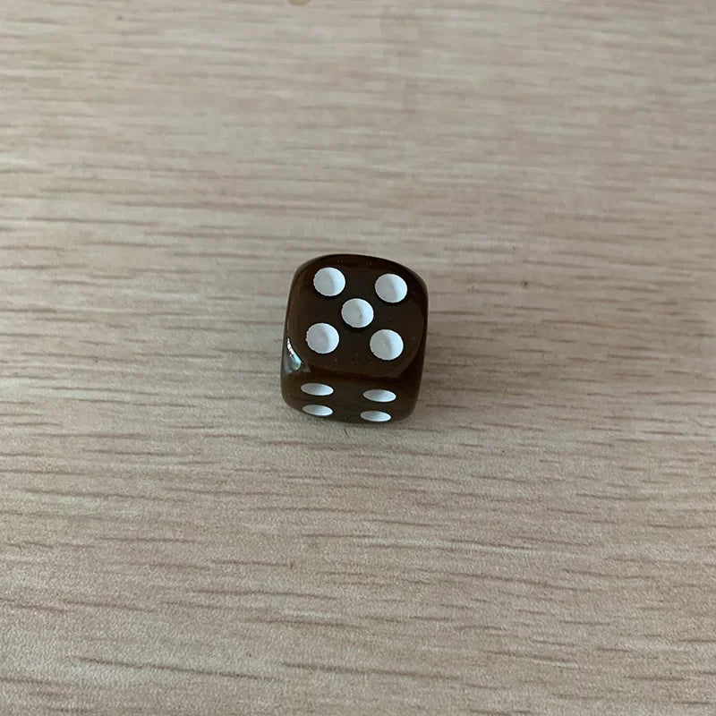 A dark brown acrylic die with white dots is placed on a light wooden surface.