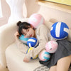 A young woman is relaxing on a sofa with a pink and blue volleyball pillow.