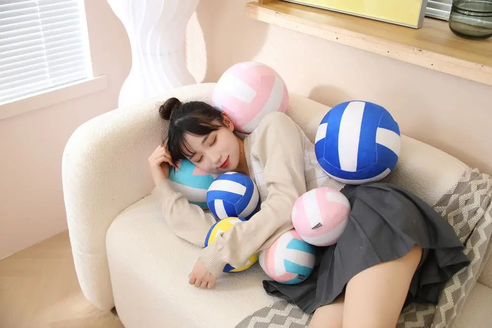 A young woman is relaxing on a sofa with a pink and blue volleyball pillow.