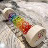 A wooden rain sound shaker toy filled with colorful plastic beads resting on a marble surface.