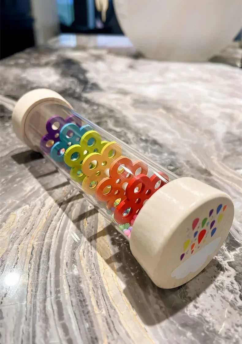 A wooden rain sound shaker toy filled with colorful plastic beads resting on a marble surface.