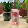 A box of red fruit ice cubes stress relief toys is displayed next to a potted green plant.