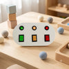 A wooden Montessori busy board for toddlers featuring colored gears, switches, and LED lights placed on a light wood table.