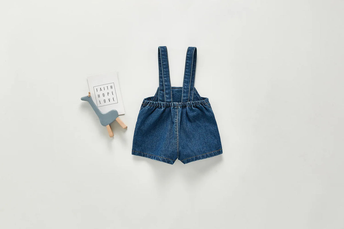 A denim romper for a toddler featuring straps and pockets, displayed on a light gray background.