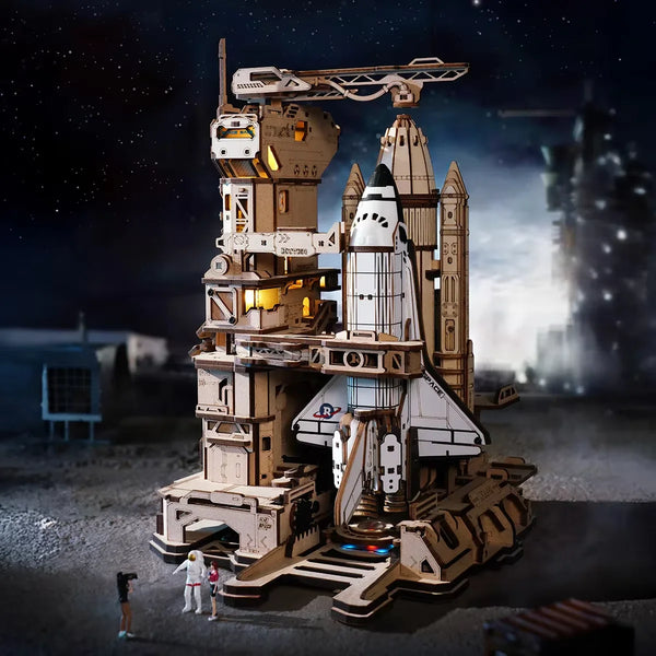 A detailed wooden model kit of a space shuttle with a launch simulator setup on a gray surface under a dark sky.