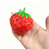 A bright red strawberry stress ball with a green leafy top is held in a person's hand.