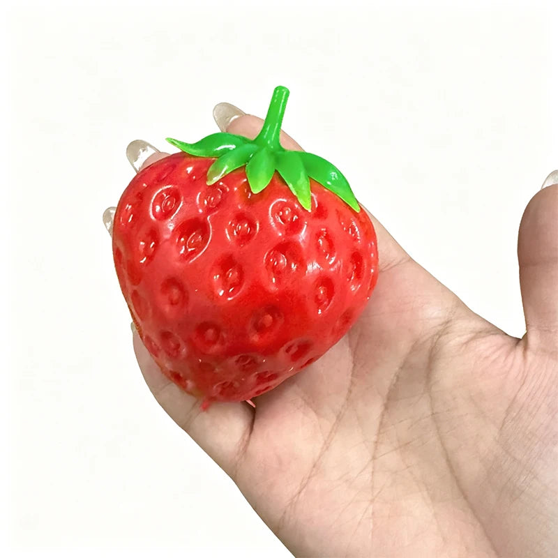 A bright red strawberry stress ball with a green leafy top is held in a person's hand.