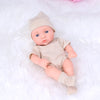A realistic soft vinyl reborn baby doll wearing a beige knitted hat and striped outfit lying on white fabric.