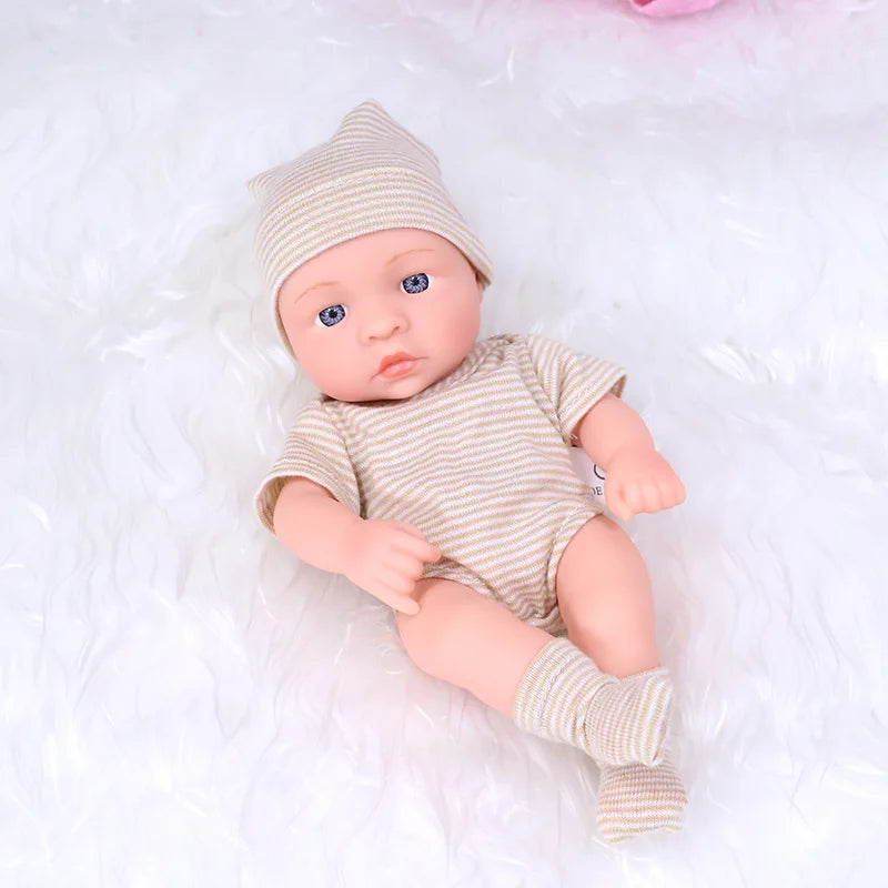 A realistic soft vinyl reborn baby doll wearing a beige knitted hat and striped outfit lying on white fabric.