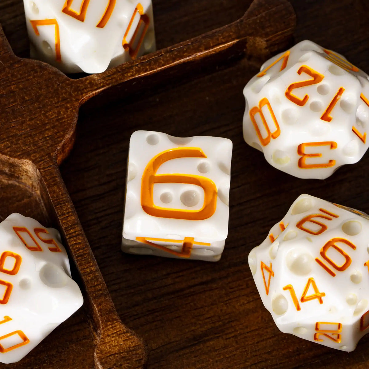 A set of seven white dice with orange numbers are displayed on a wooden surface.
