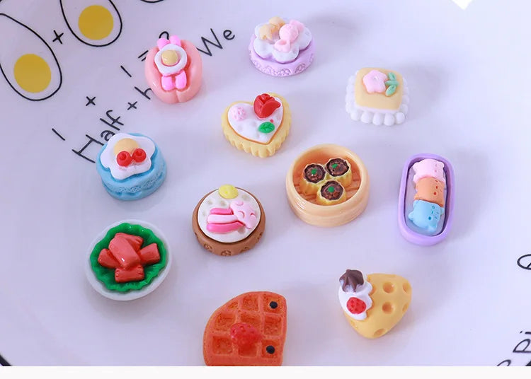 A collection of miniature dollhouse snack foods including cakes, candies, and pastries arranged on a white surface.