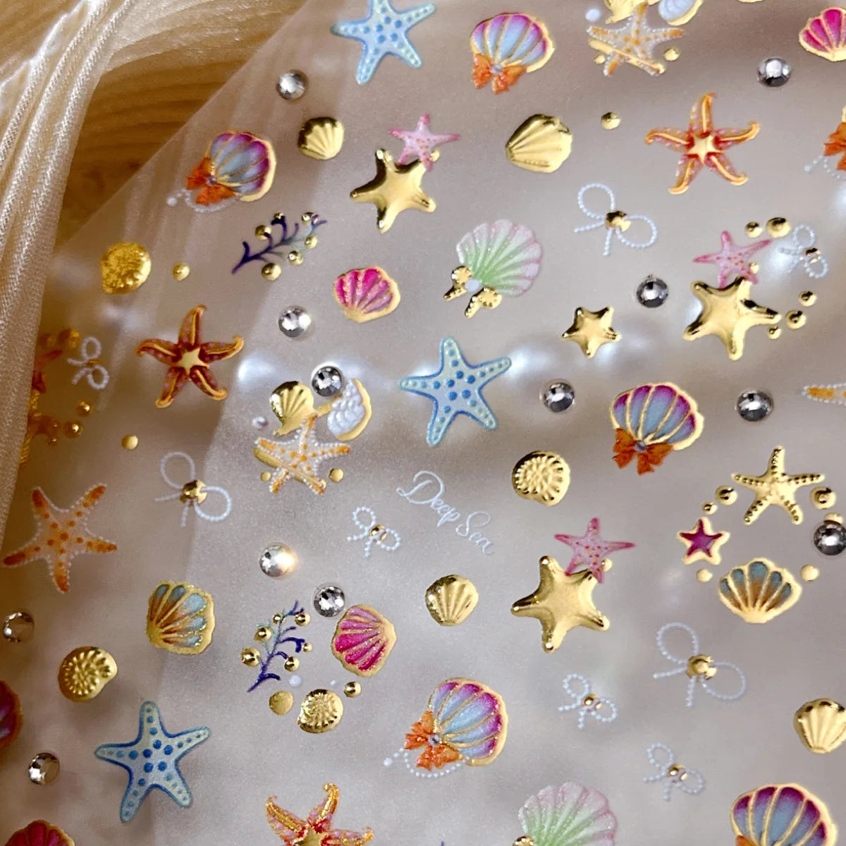 Clear sticker sheet featuring gold and iridescent starfish and seashell designs for nail art