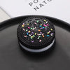 A black biscuit squishy stress relief toy with colorful sprinkles resting on a dark plate.