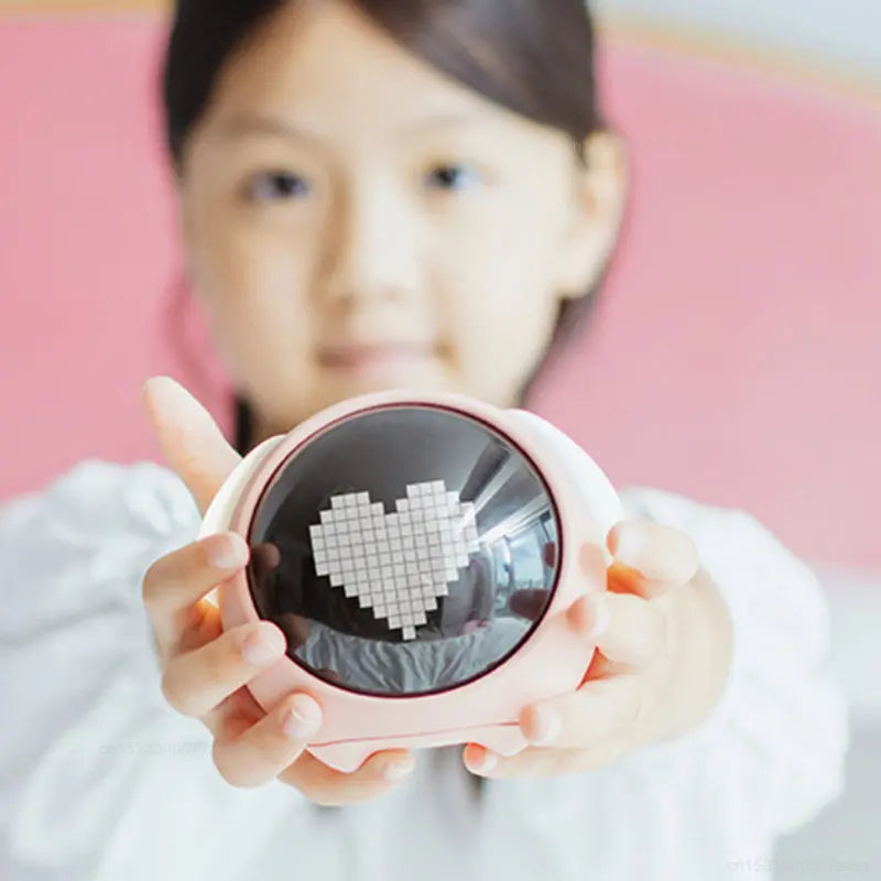A young girl holds a pink emoji alarm clock with a heart design and a night light feature.
