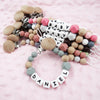 A collection of silicone teething beads and clips in various pastel colors, including pink, white, beige, and gray, arranged 