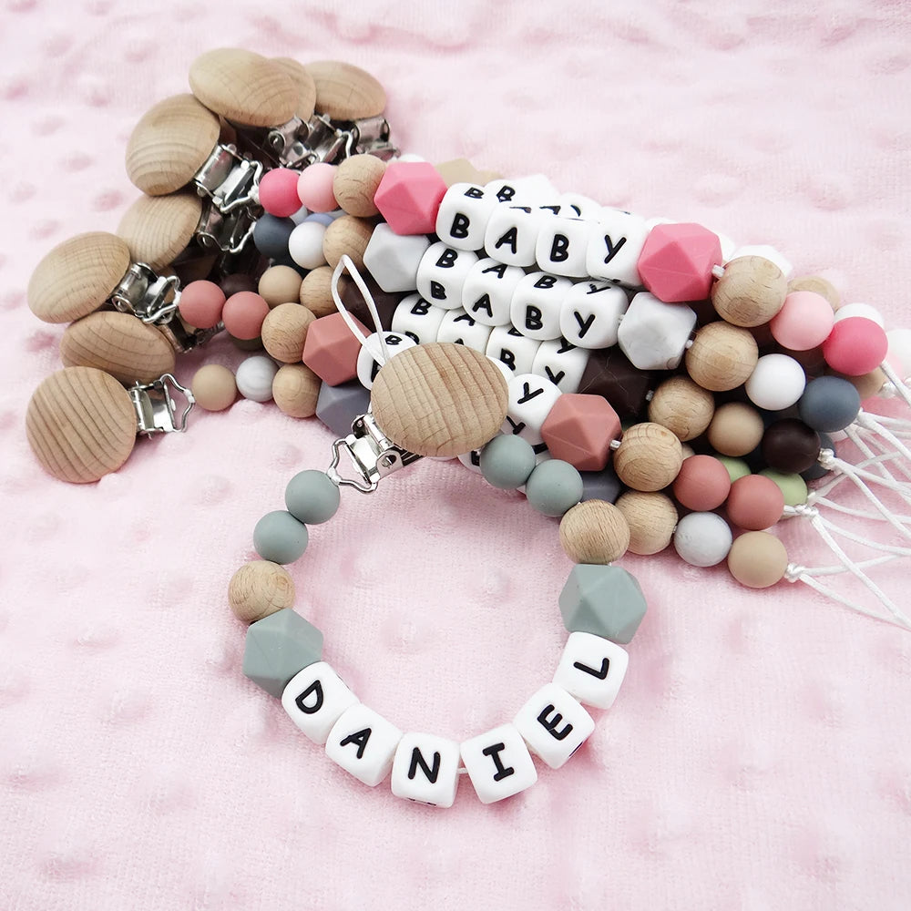 A collection of silicone teething beads and clips in various pastel colors, including pink, white, beige, and gray, arranged 