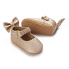 A pair of beige suede moccasin shoes for a baby girl with a decorative bow.