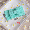 A light mint green fabric bow baby headband is displayed on a white surface with scattered daisy flowers.