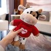 A hand is holding a red plush cow stuffed animal with white and black markings.