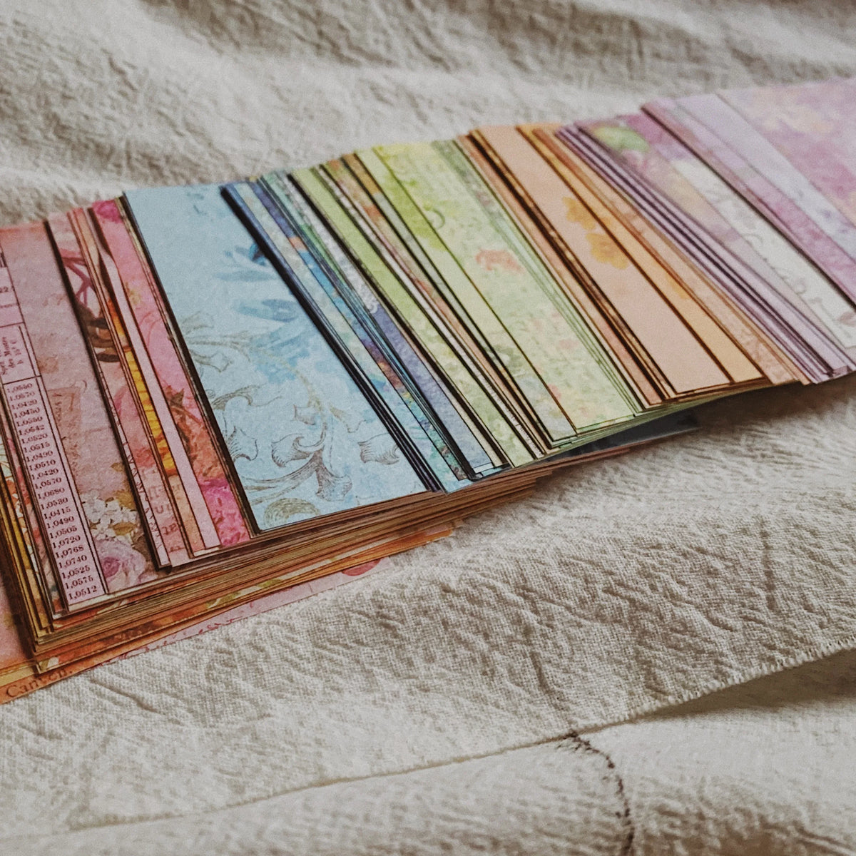 A collection of rainbow textured paper sheets in various shades and patterns laid out on a light fabric.