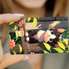 A close-up photo of a hand holding a card sticker set featuring a cute black and white cat sleeping among green leaves.