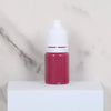 A small glass bottle of pink water marbling paint for kids sitting on a white surface.
