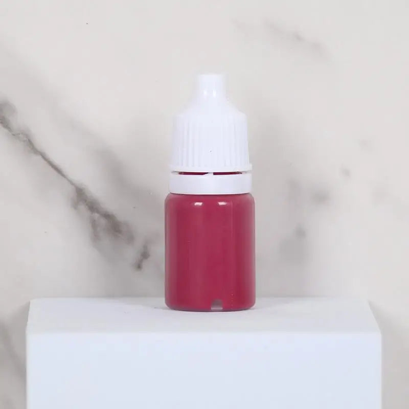 A small glass bottle of pink water marbling paint for kids sitting on a white surface.