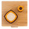 A yellow and brown crochet object is placed on a bamboo blocking board with pins and a wooden stand.