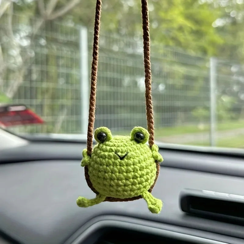 Handmade crochet green frog hanging ornament suspended from a brown string on a car interior.
