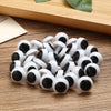 A pile of white and black plastic safety eyes for crafting, resting on a wooden surface.