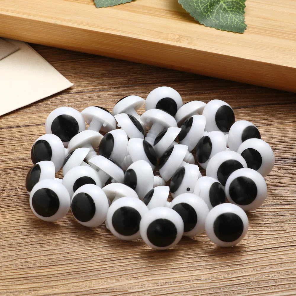 A pile of white and black plastic safety eyes for crafting, resting on a wooden surface.