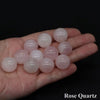A hand holds several smooth, translucent pink rose quartz crystal spheres.
