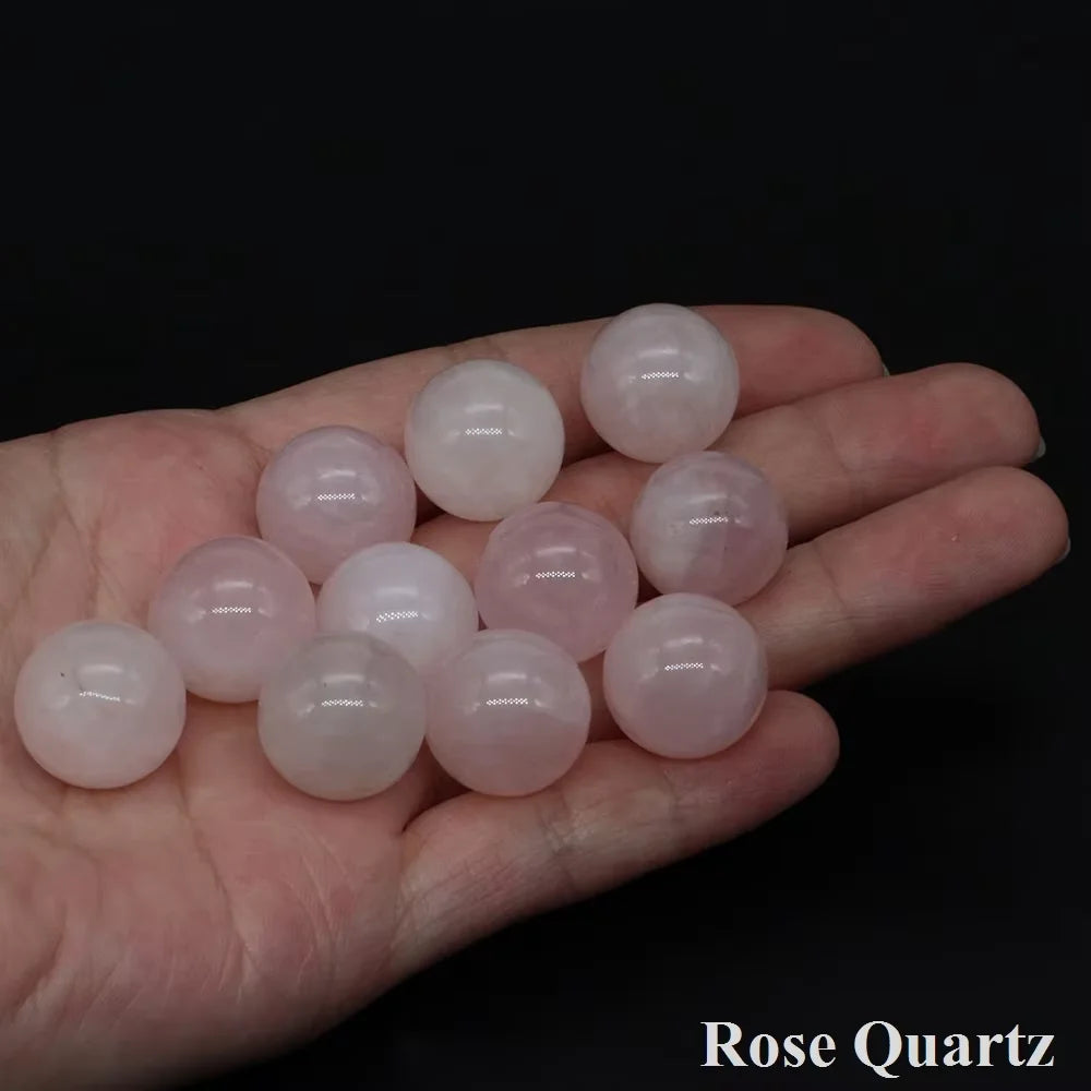 A hand holds several smooth, translucent pink rose quartz crystal spheres.