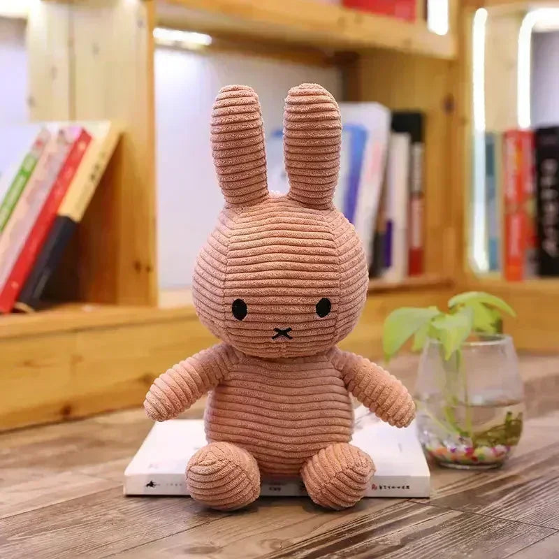 A soft, round, tan Miffy plush toy with long ears sitting on a wooden surface.